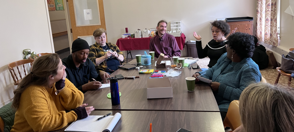 Group of people sitting around a rectangle table in a conference room and talking to each other