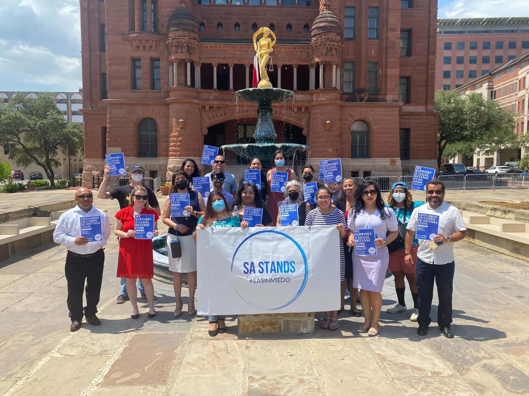 A photo of a group of people holding a sign saying "SA STANDS" in Bexar County, Texas after the creation of an immigrant legal defense fund.