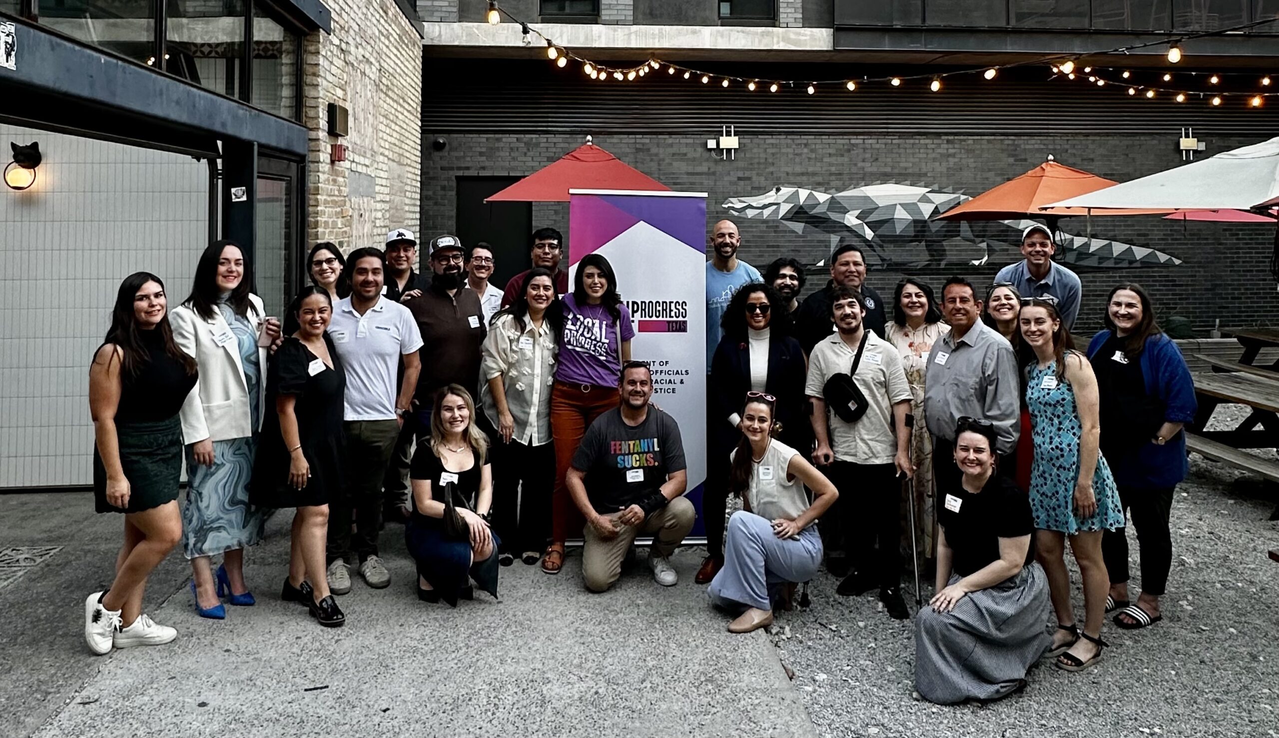 Image of LPTX members and partners posting for a photo at a meetup outside under lights.