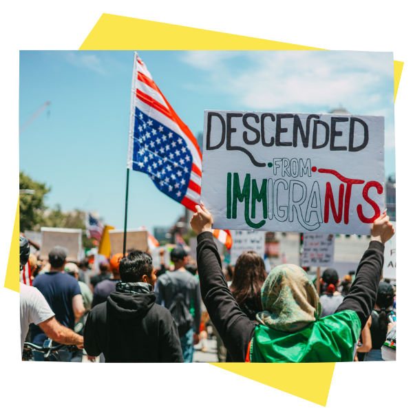 A person holds a sign at a protest that reads "Descended from Immigrants".