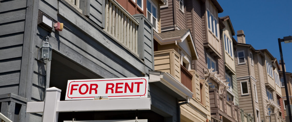 A row of townhouses with a red "For Rent" sign outside.