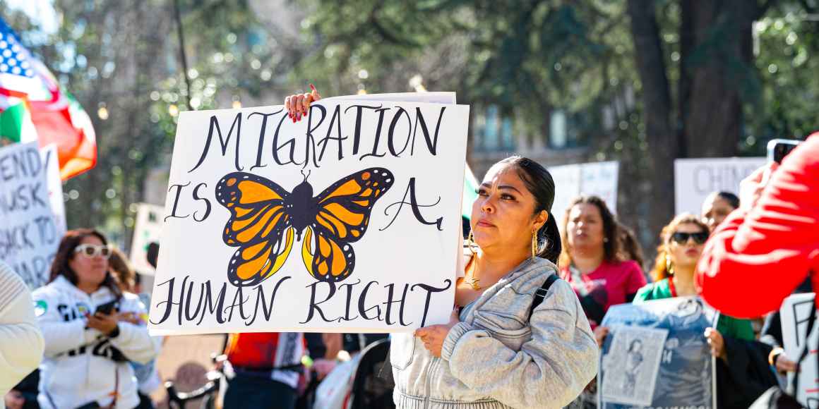 A person holding a sign that says "Migration is a human right" with a beautifully painted butterfly on it.