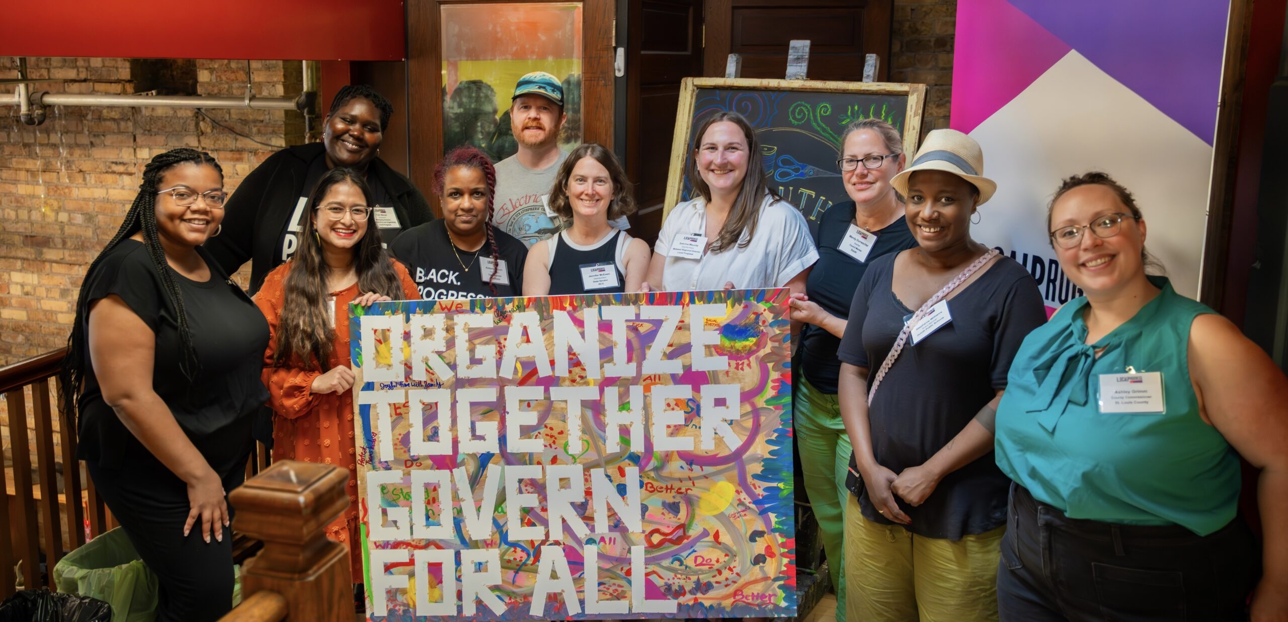LPMN members, partners, and staff taking a group photo holding up a sign that says, "ORGANIZE TOGETHER. GOVERN FOR ALL."