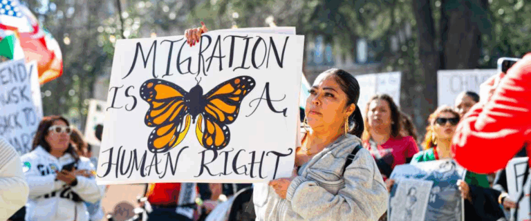A protestor holds a sign that reads "Migration is a human right"