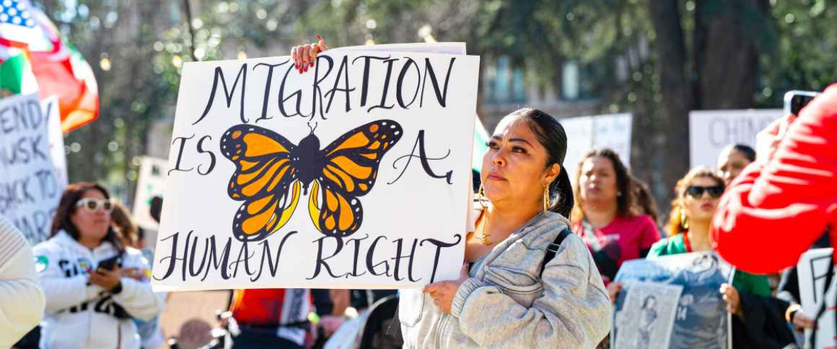 A protestor holds a sign that reads "Migration is a human right"