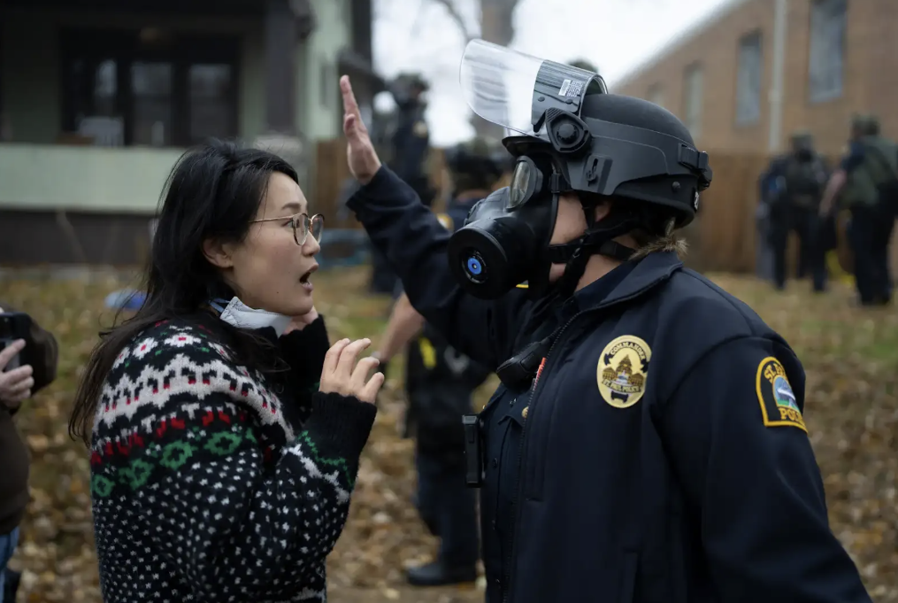 A person facing off against a masked officer.