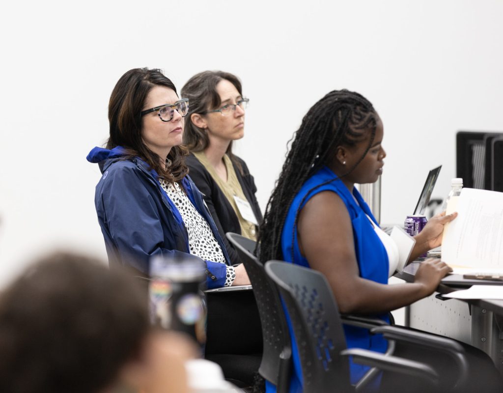 A group of 3 people at a desk listening to the panel